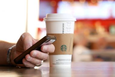 Dostum telefonuna mesaj okuma ve Starbucks sıcak içecek kahve ile içme gıda mahkeme alanda hareket insanlar bulanıklık
