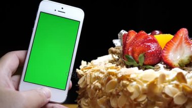 Meyve doğum günü pastası ve yeşil ekran telefon siyah bir arka plan üzerinde tutan el hareketi