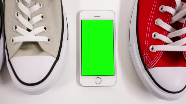 Bewegung von Displayschuhen und Grünbildtelefon auf weißem Hintergrund für Freizeitkonzept — Stockvideo