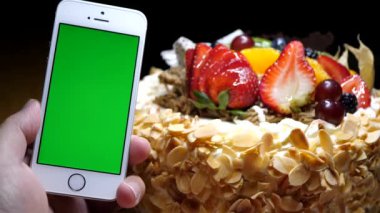 Meyve doğum günü pastası ve yeşil ekran telefon siyah bir arka plan üzerinde tutan el hareketi