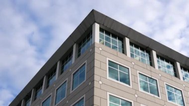 Işıklı yansıyan cam cephe üzerinde modern ofis binası ile bulutlu gökyüzü hareket