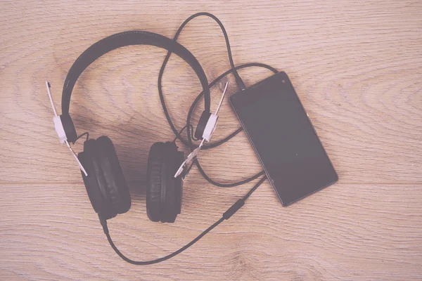 Kopfhörer und Telefon auf einer Holzoberfläche Vintage Retro-Filter. — Stockfoto