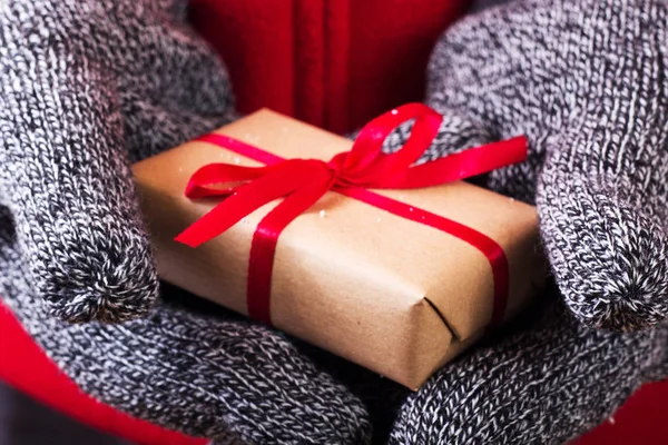 Manos abiertas sosteniendo un regalo envuelto con una cinta roja — Foto de Stock