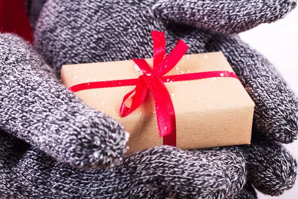 Manos abiertas sosteniendo un regalo envuelto con una cinta roja — Foto de Stock