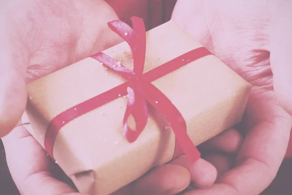 Manos abiertas sosteniendo un regalo envuelto con una cinta roja Vintage R — Foto de Stock