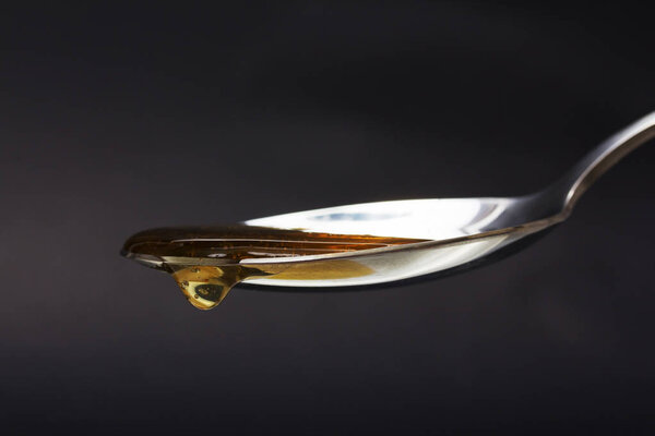 Honey pouring from spoon against a dark background