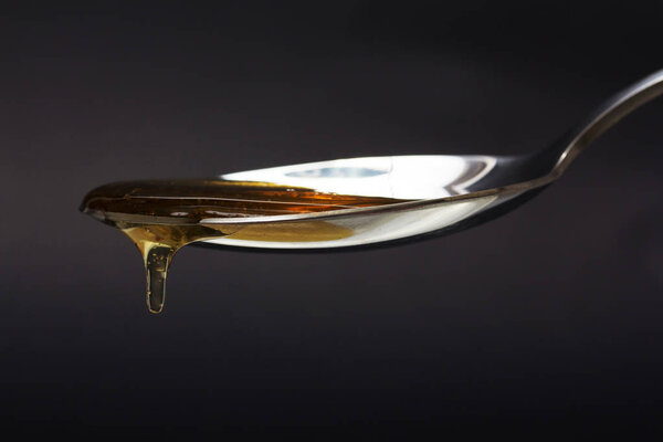 Honey pouring from spoon against a dark background