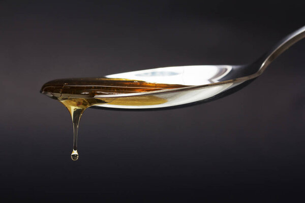 Honey pouring from spoon against a dark background