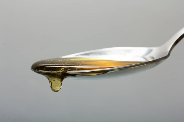 Honey pouring from spoon against a light background