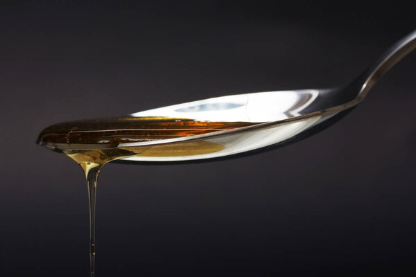 Honey pouring from spoon against a dark background