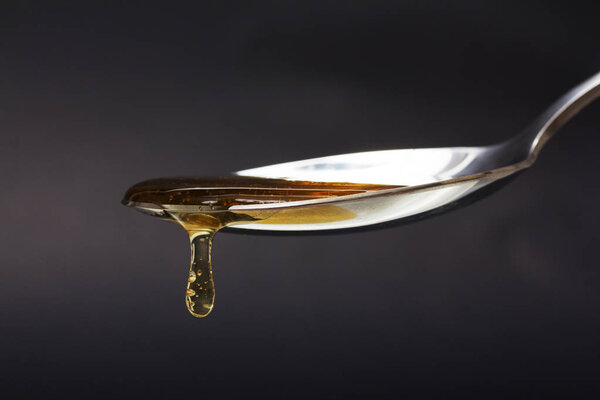 Honey pouring from spoon against a dark background