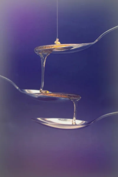 Miele versando da cucchiaio su uno sfondo scuro — Foto Stock