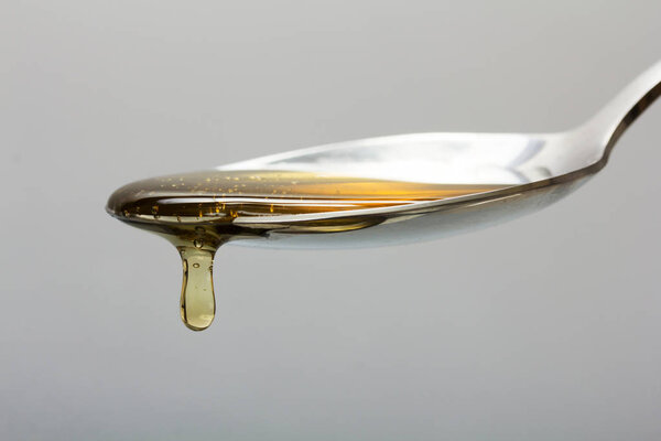 Honey pouring from spoon against a light background