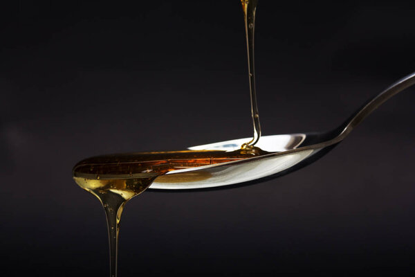 Honey pouring from spoon against a dark background
