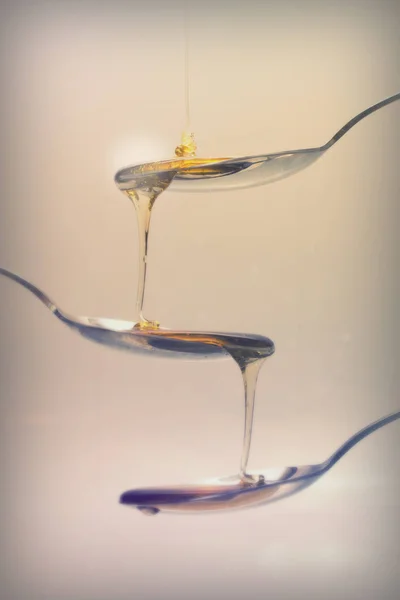 Honung hälla från sked mot ljus bakgrund — Stockfoto