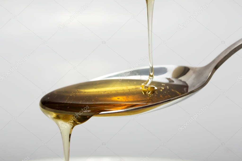 Honey pouring from spoon against a light background