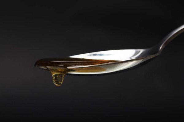 Honey pouring from spoon against a dark background