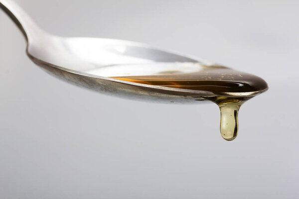 Honey pouring from spoon against a light background