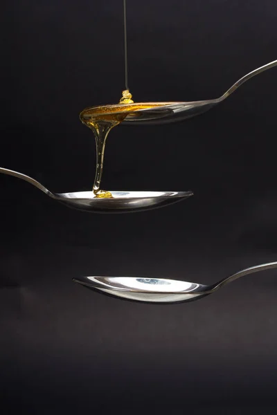 Miele versando da cucchiaio su uno sfondo scuro — Foto Stock