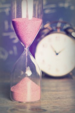 Bir kara tahta arka plan ile ahşap yüzeyde kum saati karşı