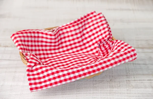 Wicker basket with a red checked fabric napkin on a wooden white table