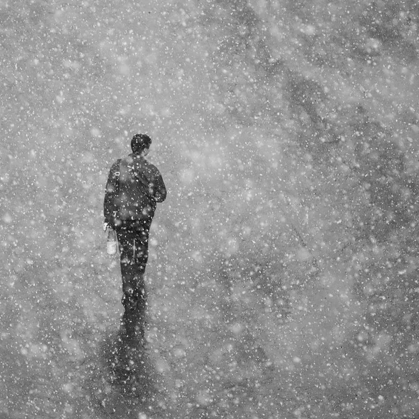 A man walks down the street. View from above. The man is walking in the snowy weather.