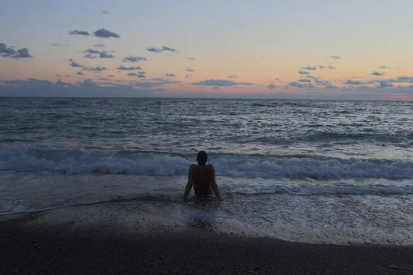 Gün batımında deniz kenarında oturan adam. 