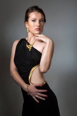 Glamour yarım uzunlukta, koyu gri arka plan üzerinde siyah elbise giymiş seksi genç esmer kadın. 