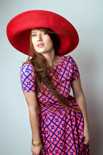 Fashion Brunette Lady in red hat and red blue dress on white grey background. studio