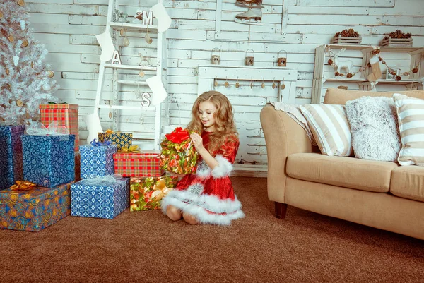 Santa dívka držící vánoční dárky. šťastná žena v santa hat vypadající otevírací vánoční dárek — Stock fotografie