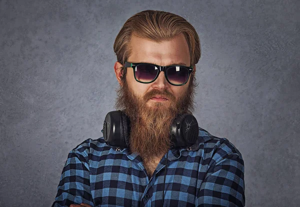 Bearded man wearing sunglasses and headphones. Studio shot on grey background — Stock Photo, Image