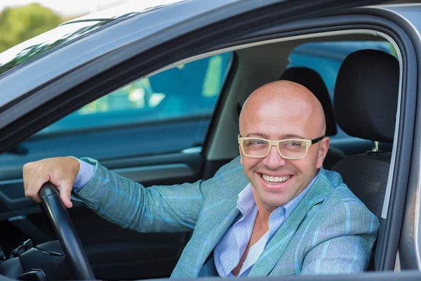 Hombre guapo sonrisa en la cara sentado en su coche, las manos en el volante — Foto de Stock