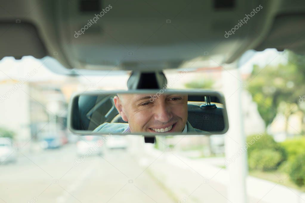 Closeup portrait, happy young man driver looking at rear view mi