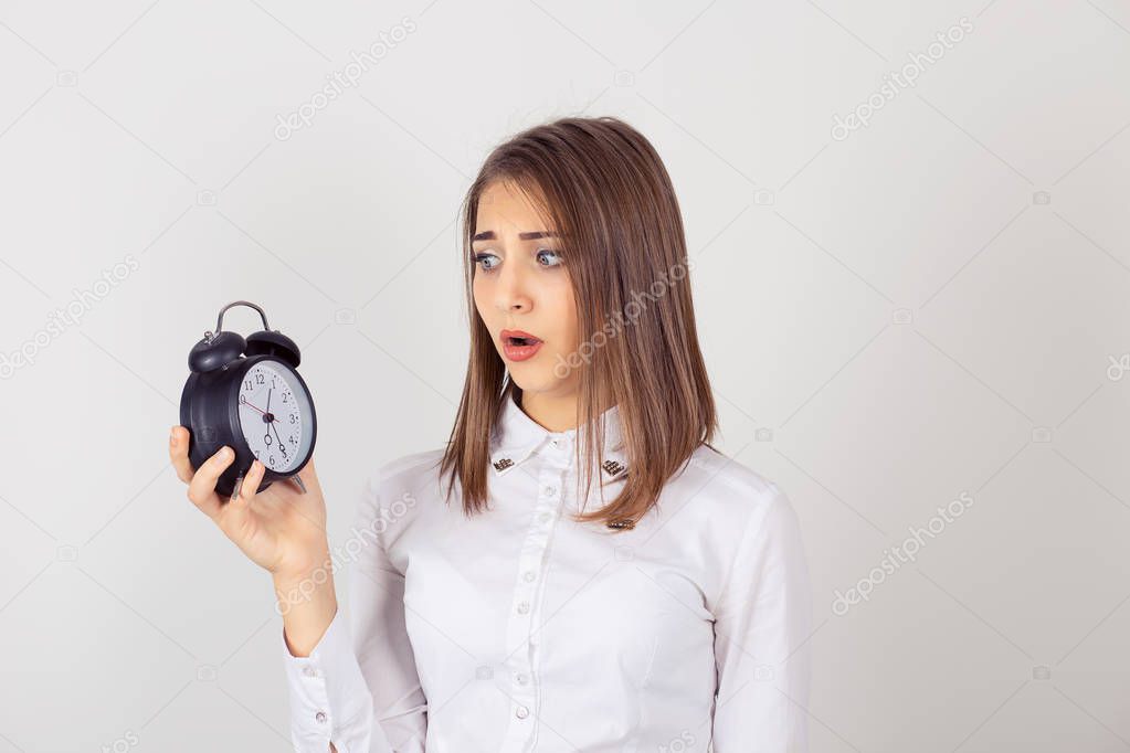 headshot young business woman with alarm clock in hand isolated white grey wall