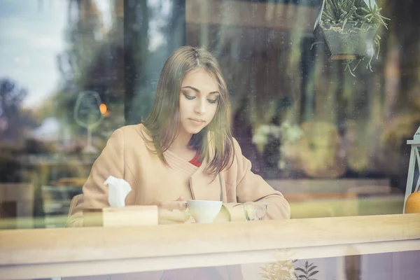 Mujer bebiendo té y mirando cuidadosamente por el escaparate de la cafetería — Foto de Stock