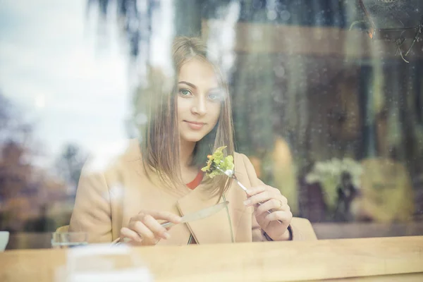 Mujer comiendo ensalada en cafetería sentada junto a la ventana sonriendo mirándote cámara . —  Fotos de Stock