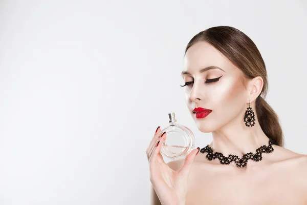 Perfume. Hermosa mujer gran maquillaje labios rojos y uñas, pestañas negras huele aroma perfume aislado fondo blanco — Foto de Stock