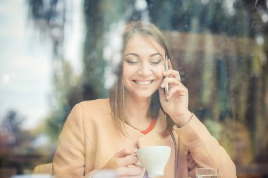 Genç kadın kahve içme ve mobil ph üzerinde konuşurken Café