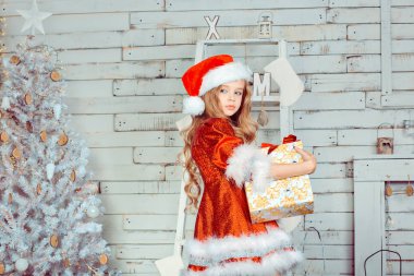 Kız gidiyor hediye ile mutlu. Kırmızı elbise ve şapka Noel ağacının yanındaki giyen çocuk. Yeni yıl. Tatil ve eğlence. Mutlu Noeller