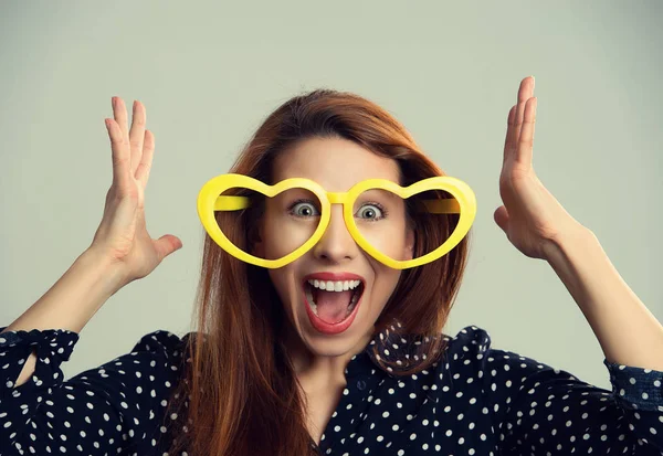 Mulher com coração em forma de óculos de festa feliz surpreendido mãos no ar — Fotografia de Stock