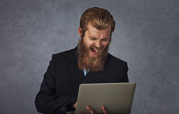 Barbudo hombre de negocios sosteniendo computadora gritando aislado gris fondo — Foto de Stock