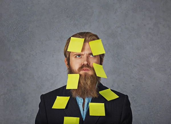 Sobrecarregado barbudo homem de negócios cheio de adesivos olhando para cima tentando se lembrar de seus planos — Fotografia de Stock