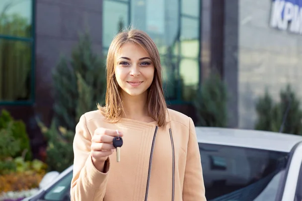 Крупним планом портрет щасливої жінки, покупець біля її нової машини показує ключ — стокове фото