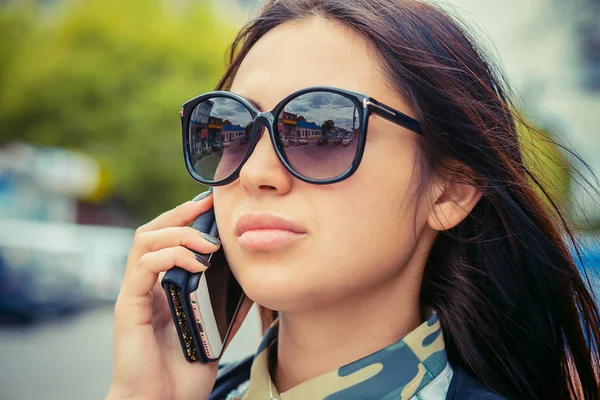 Η γυναίκα μιλάμε στο τηλέφωνο. Πόλη προβληματισμό σχετικά με γυαλιά ηλίου — Φωτογραφία Αρχείου