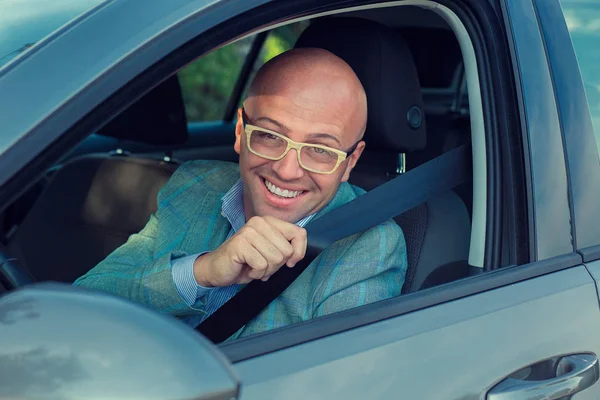 Hombre guapo sonriendo mirando a la cámara en su coche pidiendo que le muestre a abrocharse el cinturón de seguridad. Transporte seguro y concepto de vehículo . — Foto de Stock