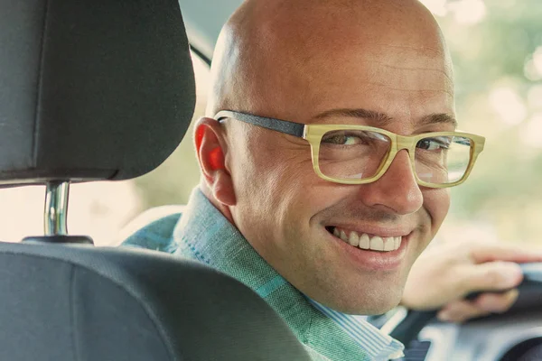 Hombre en coche nuevo manos en el volante, dando la vuelta, sonriendo mirando, hablando con los pasajeros sentados en el asiento trasero — Foto de Stock