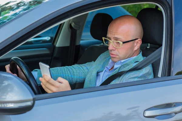 Man sitting in car with mobile phone in hand texting while driving. — Stock Photo, Image