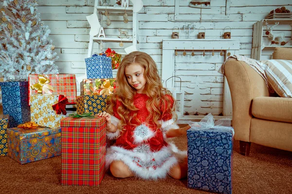 Dziewczyna stara się zdecydować, jaki prezent do wyboru ponad tło pokoju Boże Narodzenie udekorowane — Zdjęcie stockowe