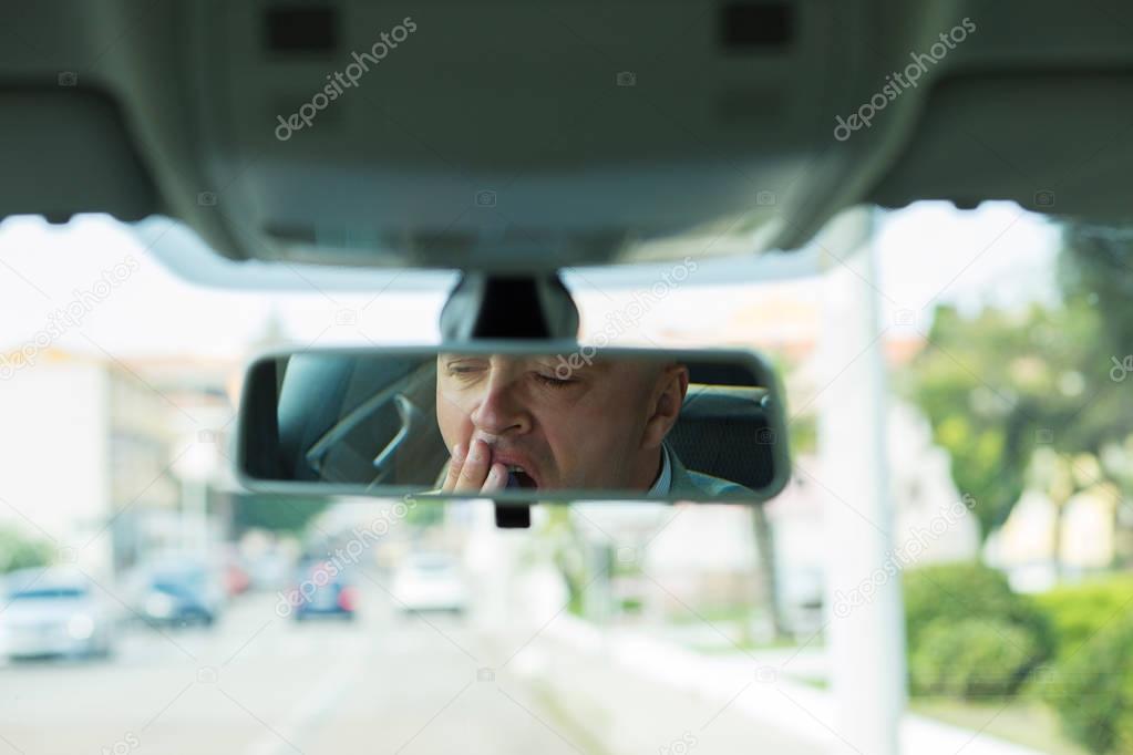 Rear mirror view reflection sleepy tired fatigued yawning exhausted young business man driving