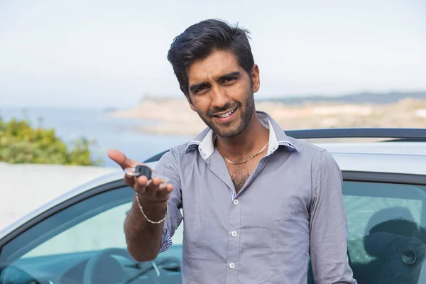 Feliz hombre sonriente sosteniendo las llaves del coche ofreciendo un coche nuevo en un fondo marino junto al mar — Foto de Stock